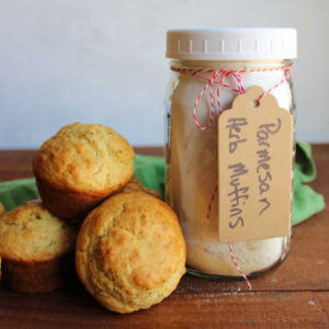 Jar of homemade parmesan herb muffin mix next to a small pile of freshly baked savory muffins.