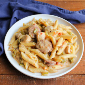 Plate of pastalaya with penne in lightly cheesy sauce with sausage, chicken, peppers, onion, and celery, ready to eat.