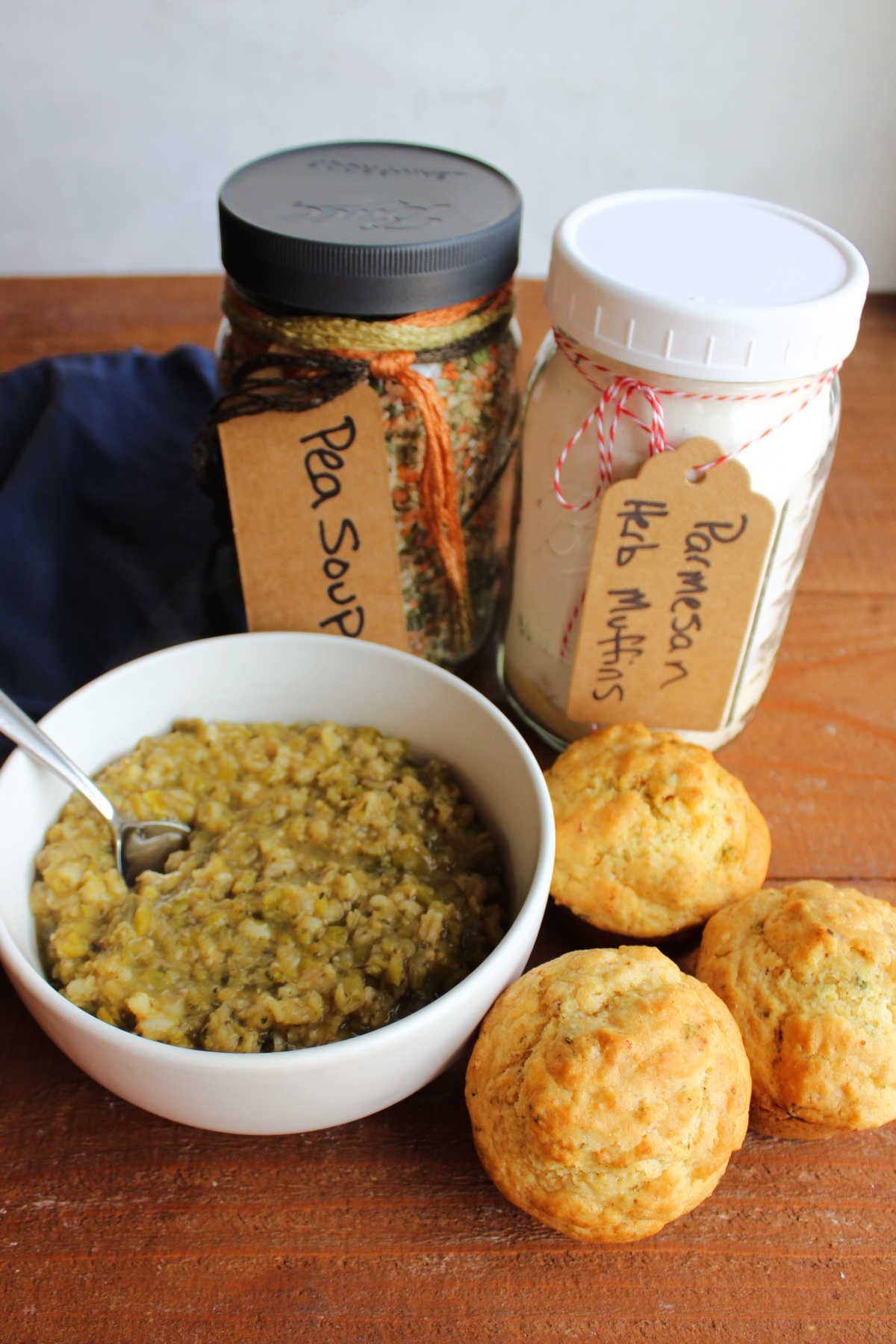 Jar of parmesan herb muffin mix next to a jar of pea soup mix with a bowl of soup and freshly baked muffins nearby. 