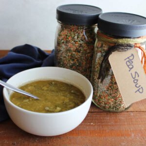 Two jars of homemade pea soup mix next to a bowl of pea soup with pearled barley and lentils.