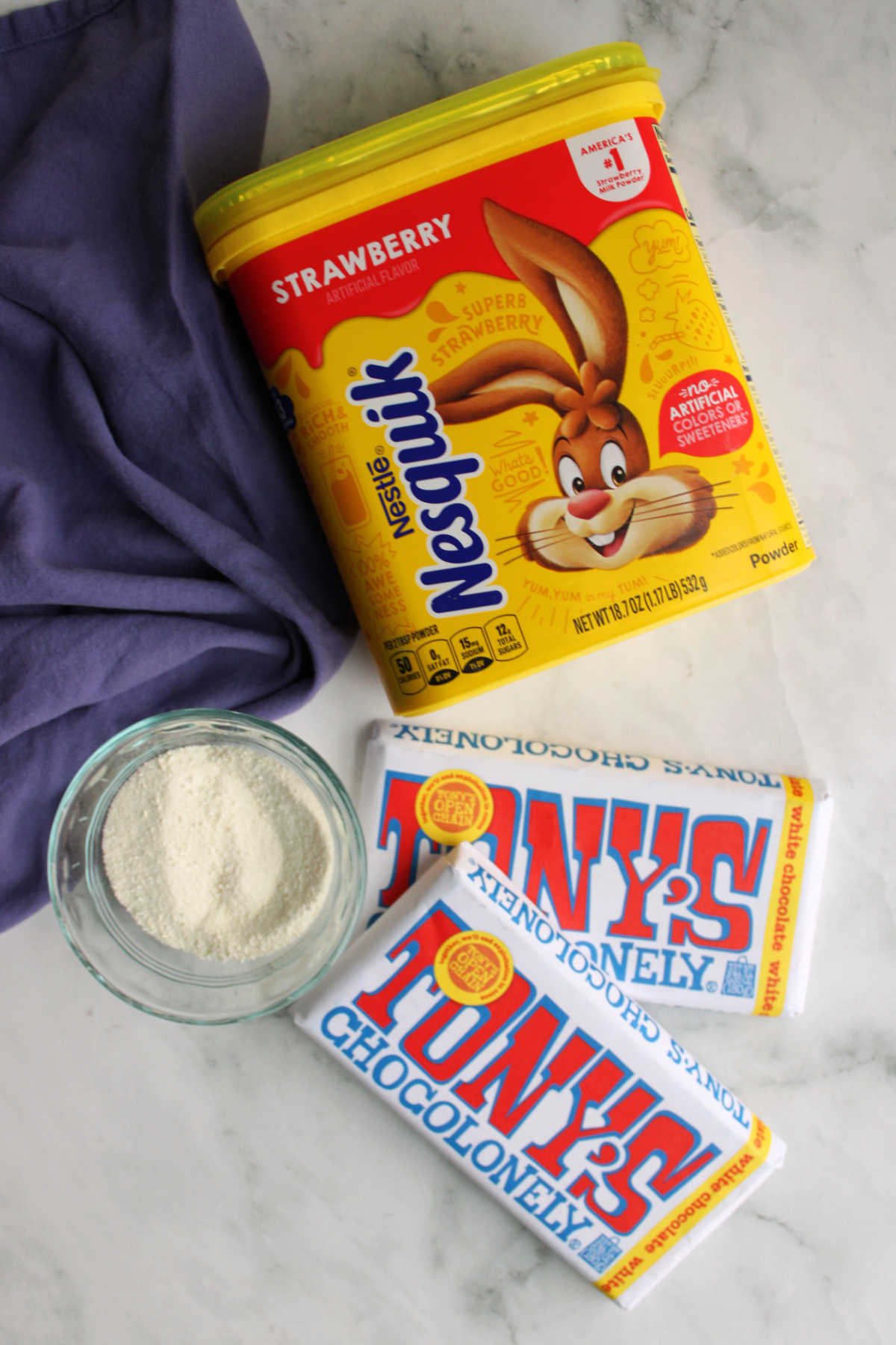Ingredients including white chocolate bars, powdered milk, and strawberry nesquick ready to be made into strawberry hot chocolate mix. 