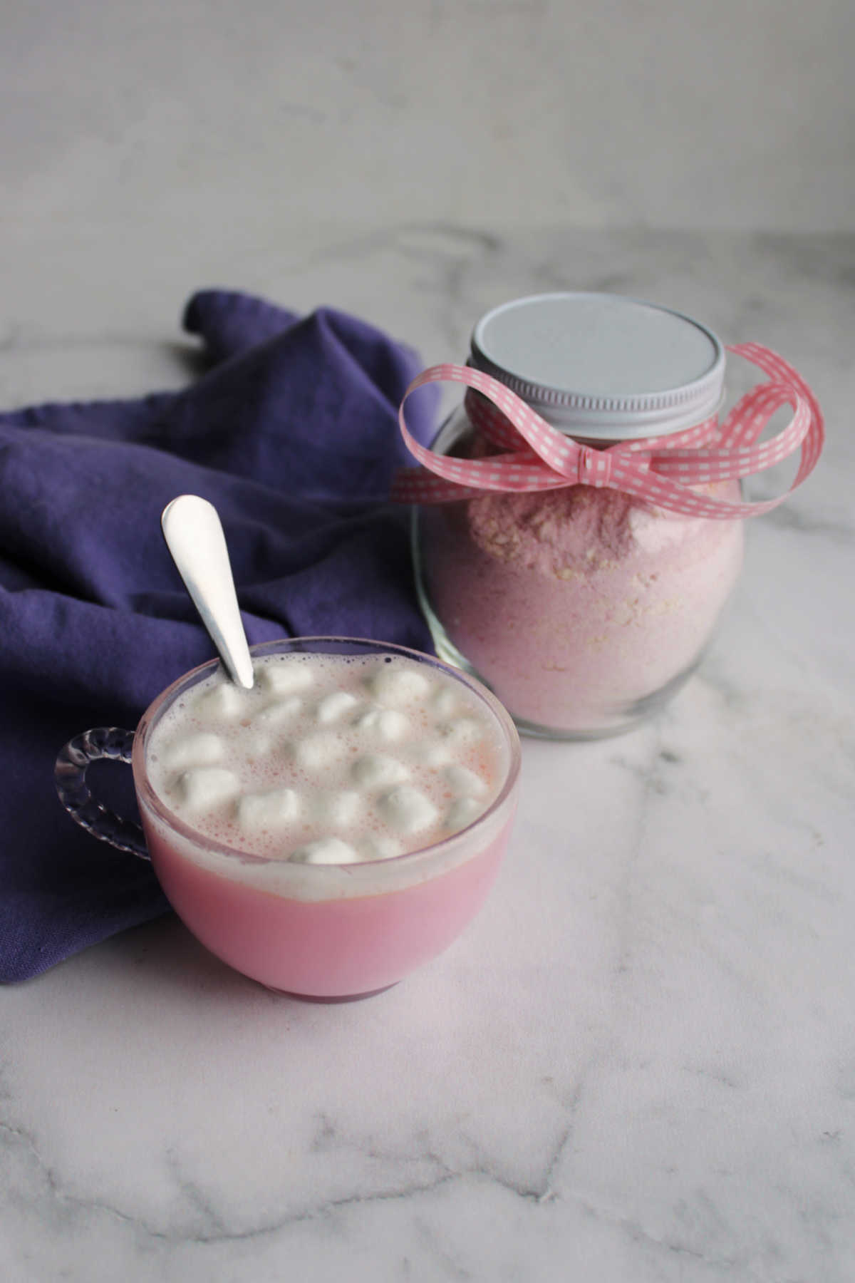 Glass mug of strawberry hot chocolate next to jar of homemade hot chocolate mix with pink bow on it. 