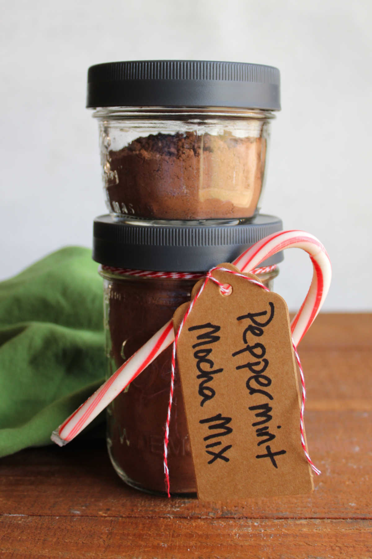 Pint jar filled with peppermint mocha mix with a gift tag and candy cane tied to it topped with a smaller jar with more coffee mix inside. 