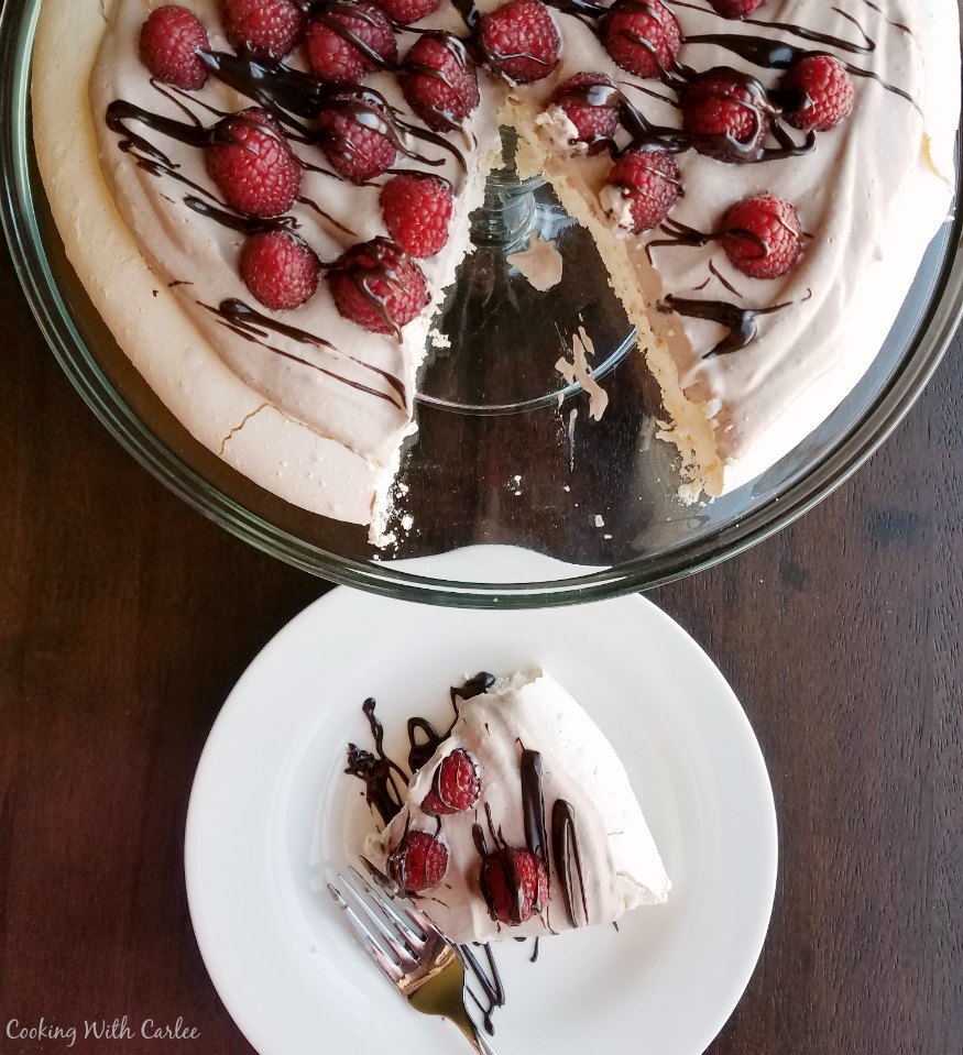 Large pavlova on glass cake stand with a slice on a dessert plate nearby. 