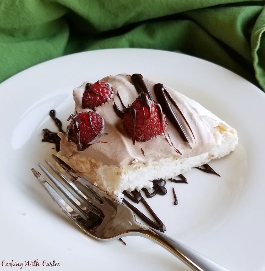 Fork next to a slice of pavlova with fluffy white meringue, chocolate whipped cream, raspberries, and a drizzle of chocolate. 