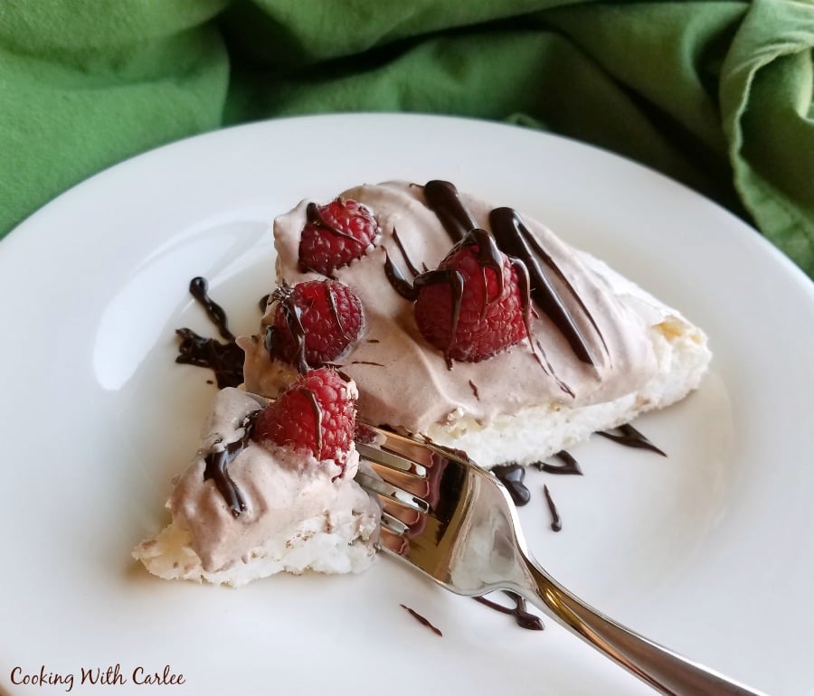 Fork getting a bite of pavlova with chocolate whipped cream and raspberries on top. 