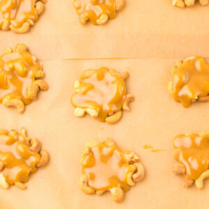 Dollops of caramel and cashews on parchment paper lined pan, waiting for their chocolate topping.