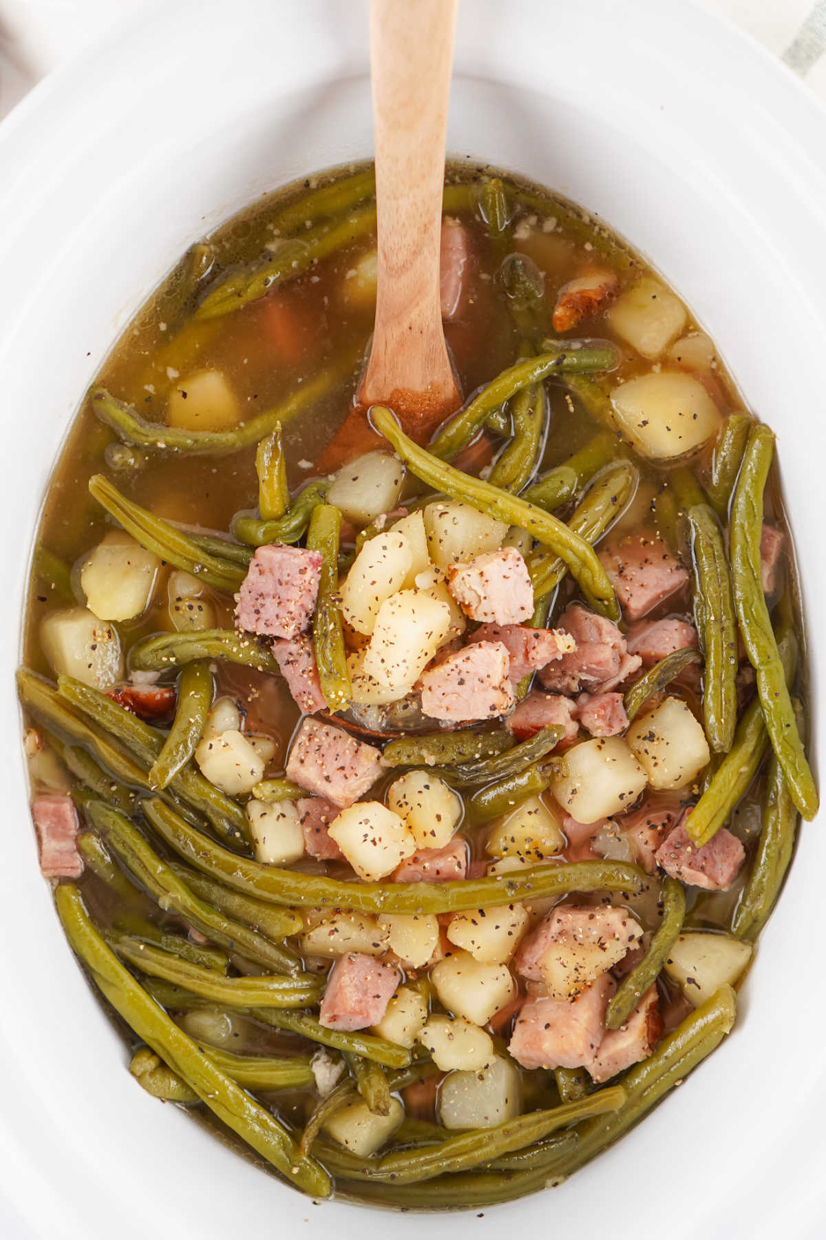 Crockpot Green Beans With Ham and Potatoes 6 Crockpot filled with green beans with chunks of ham and potatoes in a well seasoned broth.