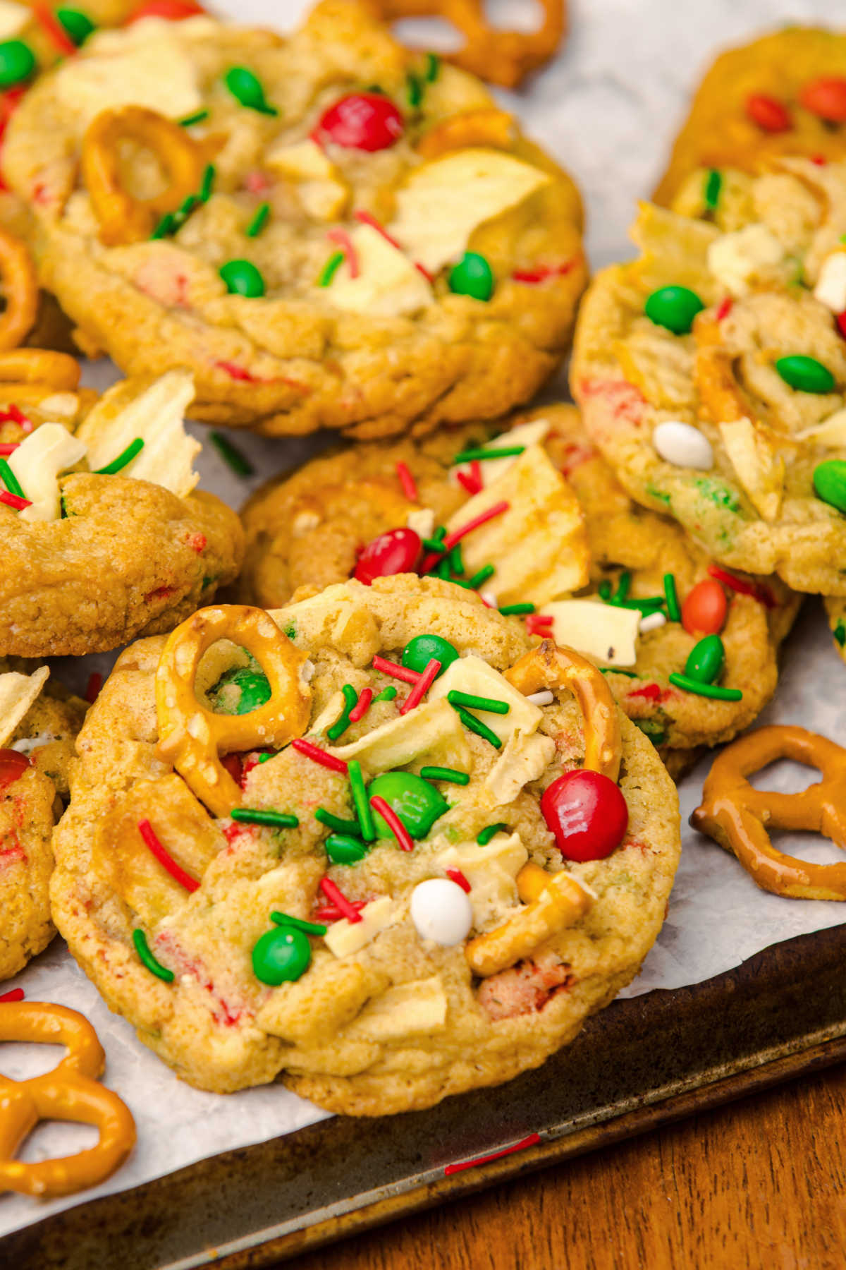 Tray of baked kitchen sink cookies filled with Christmas colored candies, sprinkles, pretzels, potato chips, and chocolate chunks, ready to eat. 
