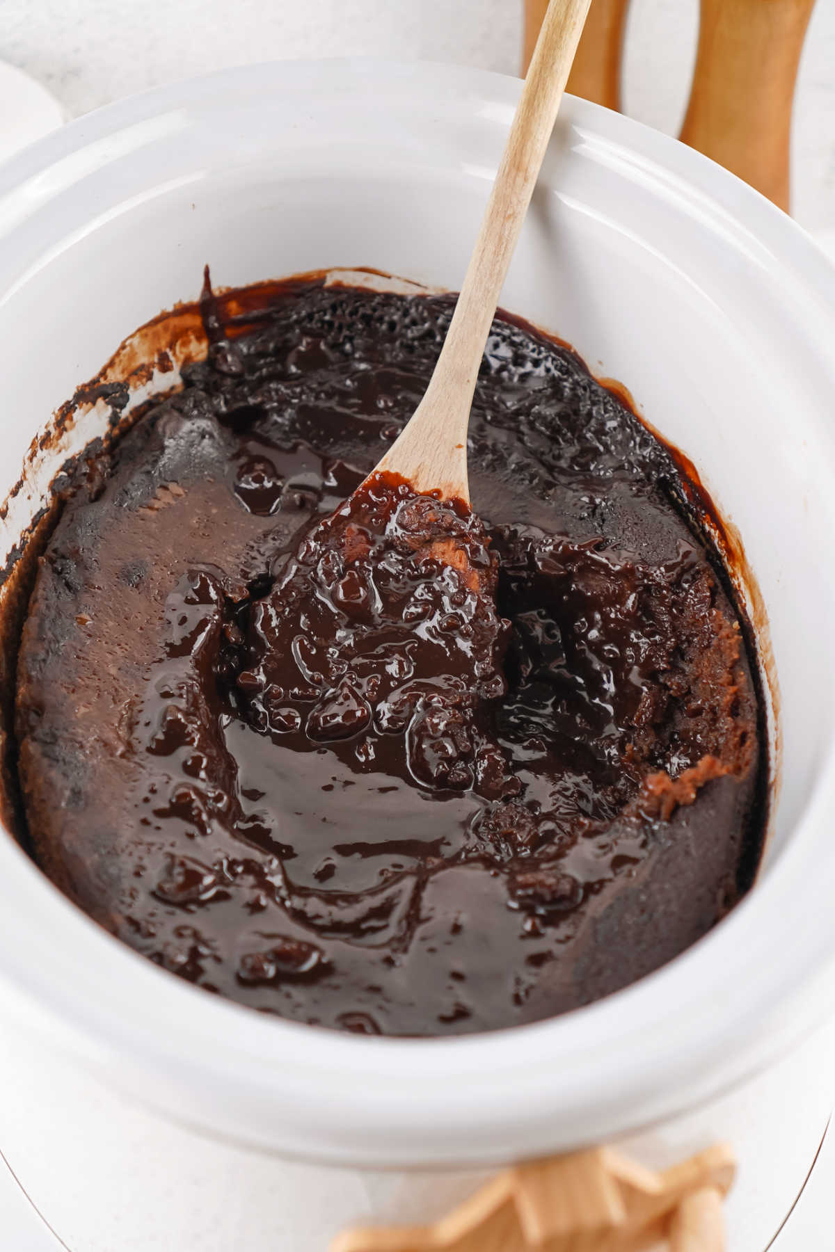 Crockpot Chocolate Cobbler 8 Crockpot with wooden spoon broken through the chocolate cobbler showing cakey layer on top and rich chocolate pudding layer underneath.