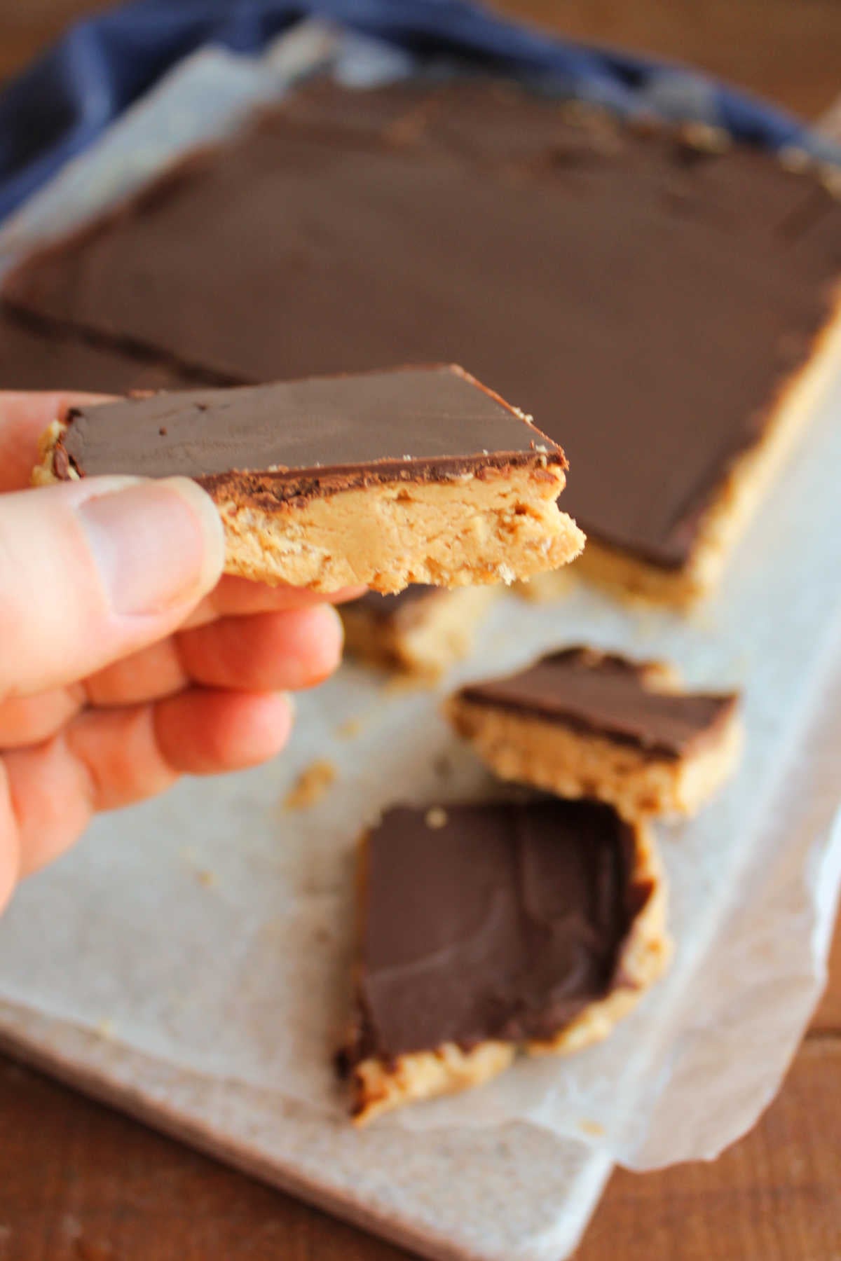 Hand holding a crunchy buckeye bar with rice krispies in the peanut butter layer and a thin layer of chocolate on top. 