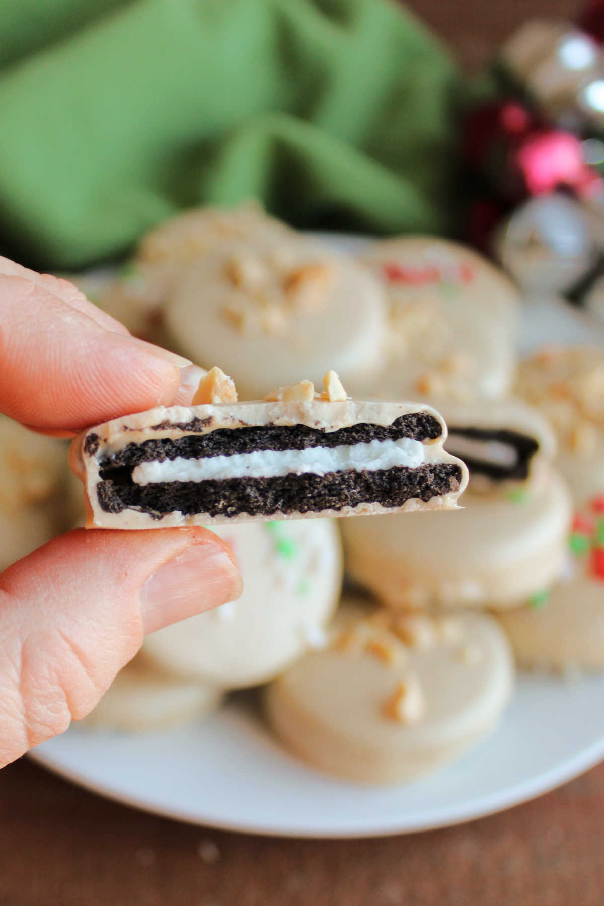 Hand holding a half of a peanut butter dipped Oreo showing thin peanut butter candy coating around the chocolate sandwich cookie. 