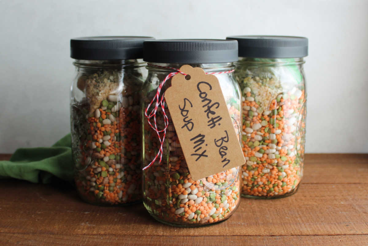 Confetti Bean Soup Mix In A Jar 6 3 quart jars filled with bean soup mix made up of different kinds of beans with a baggie of spice mix on top, ready to be gifted.