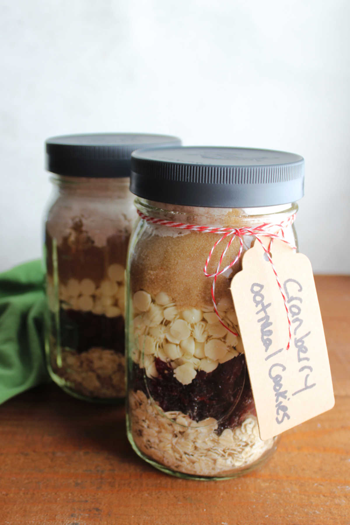 Glass quart jars filled with layers of oatmeal, craisins, white chocolate chips, brown sugar, sugar, and flour mixture with tag that says cranberry oatmeal cookies. 