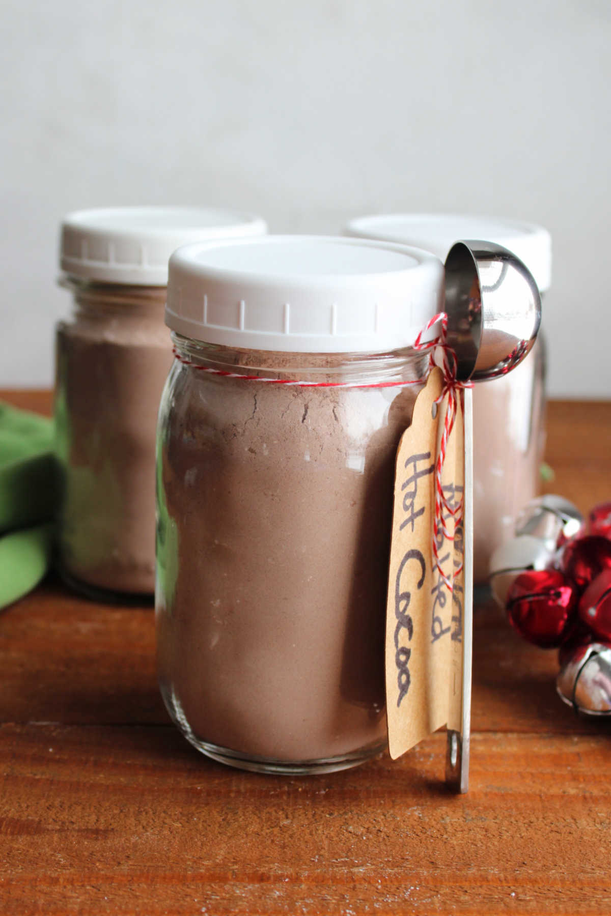 Three glass pint jars filled with malted hot chocolate mix with a tag and measuring spoon tied to one, ready to be given as a homemade edible gift. 