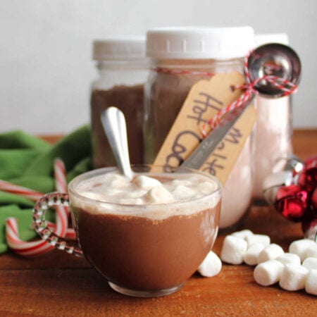Glass mug of malted hot cocoa with mini marshmallows on top with jars of more homemade malted hot cocoa mix in the background.