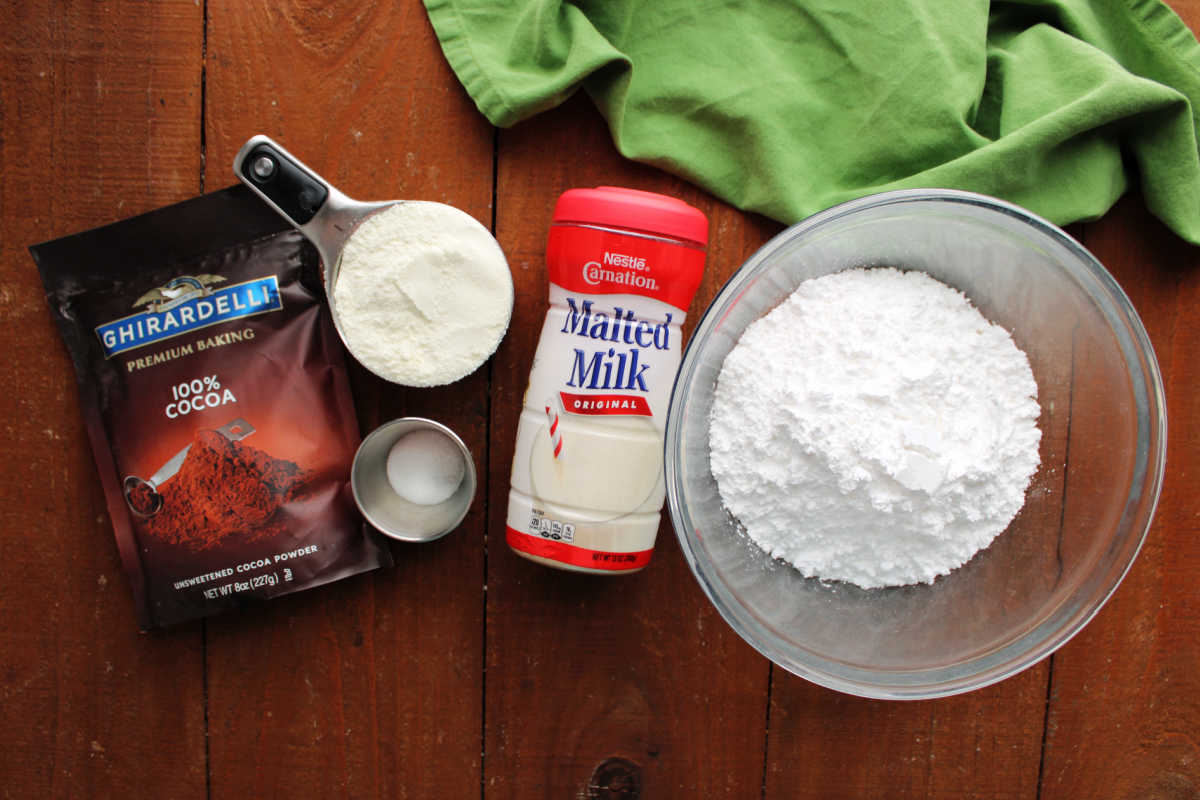 Ingredients including cocoa powder, milk powder, salt, malted milk powder, and powdered sugar ready to be made into malted hot chocolate mix. 