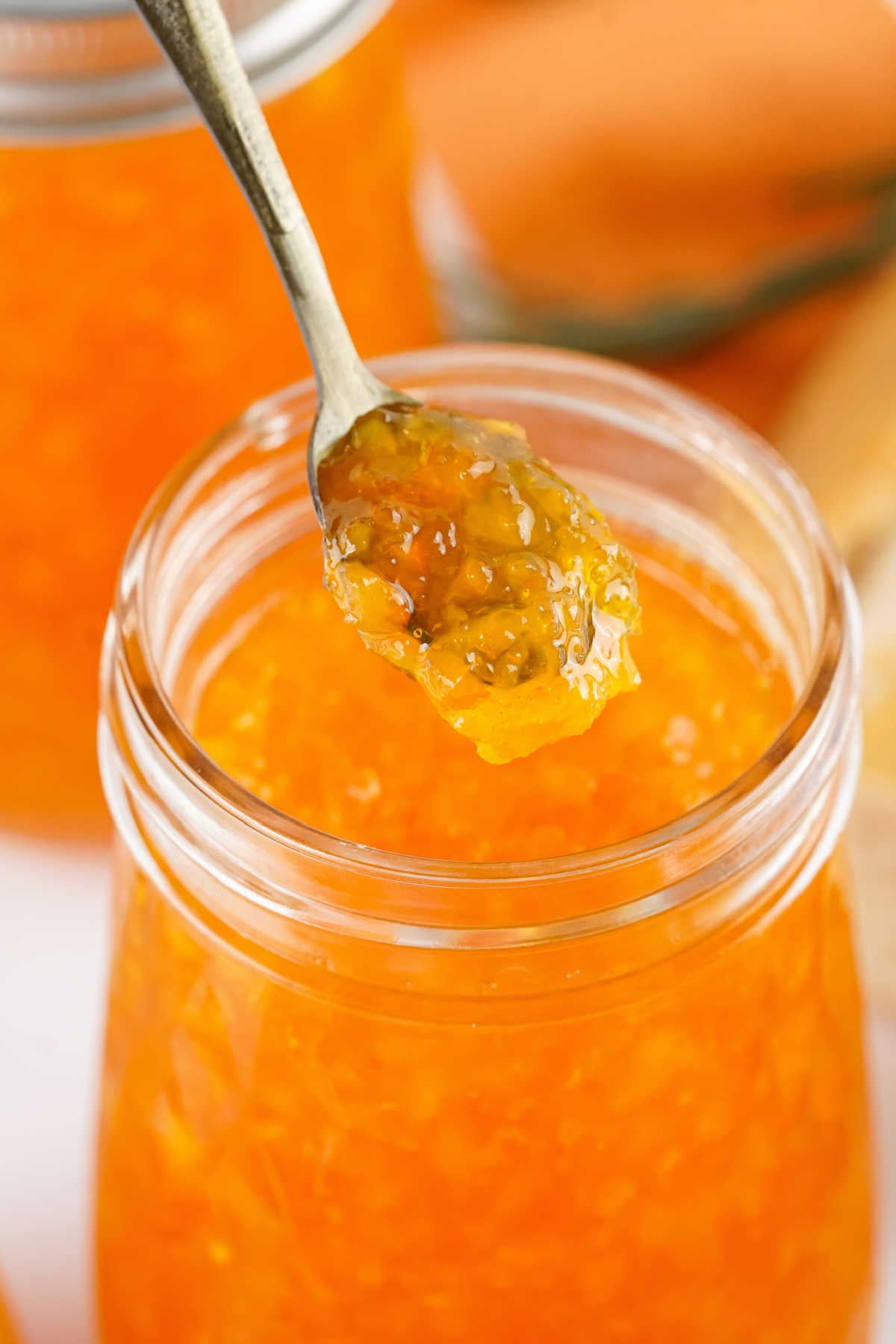 Spoon lifting out a scoop of thick homemade orange marmalade with flecks of orange rind inside. 