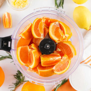 Chunks of fresh orange in a food processor, ready to be processed down.