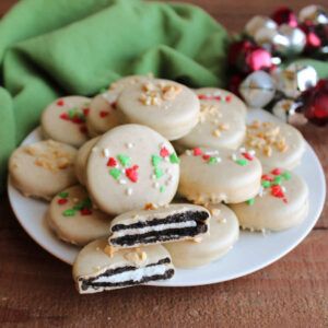 Plate of Oreos dipped in peanut butter candy coating topped with chopped nuts and Christmas sprinkles.