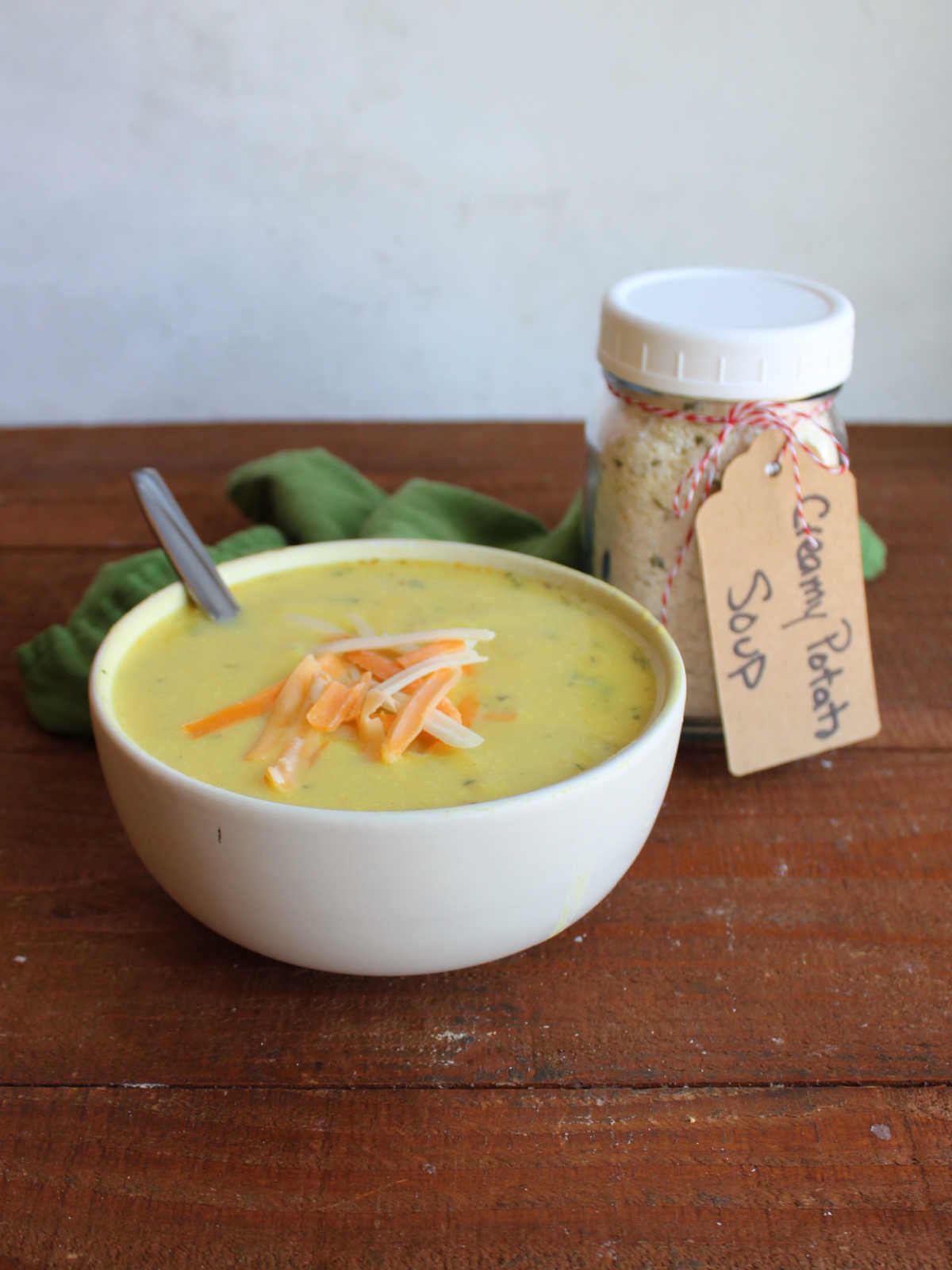 Bowl of creamy potato soup topped with shredded cheese next to a jar of homemade potato soup mix that made the soup. 