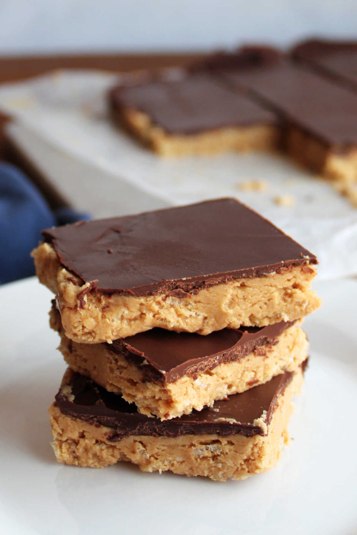 Stack of crunchy peanut butter bars with Rice Krispies in the peanut butter layer and a chocolate shell on top. 