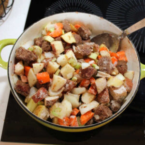 Pot of browned venison chunks and veggies coated in extra flour mixture, ready to add the liquid for the stew.