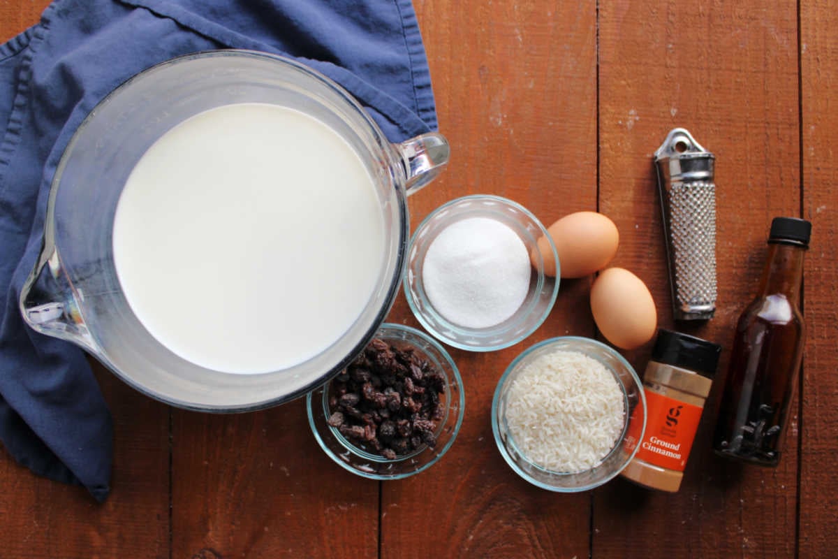Baked Rice Pudding With Uncooked Rice 7 Ingredients including milk, eggs, sugar, uncooked rice, raisins, cinnamon, nutmeg, and vanilla extract ready to be made into old fashioned baked rice pudding.