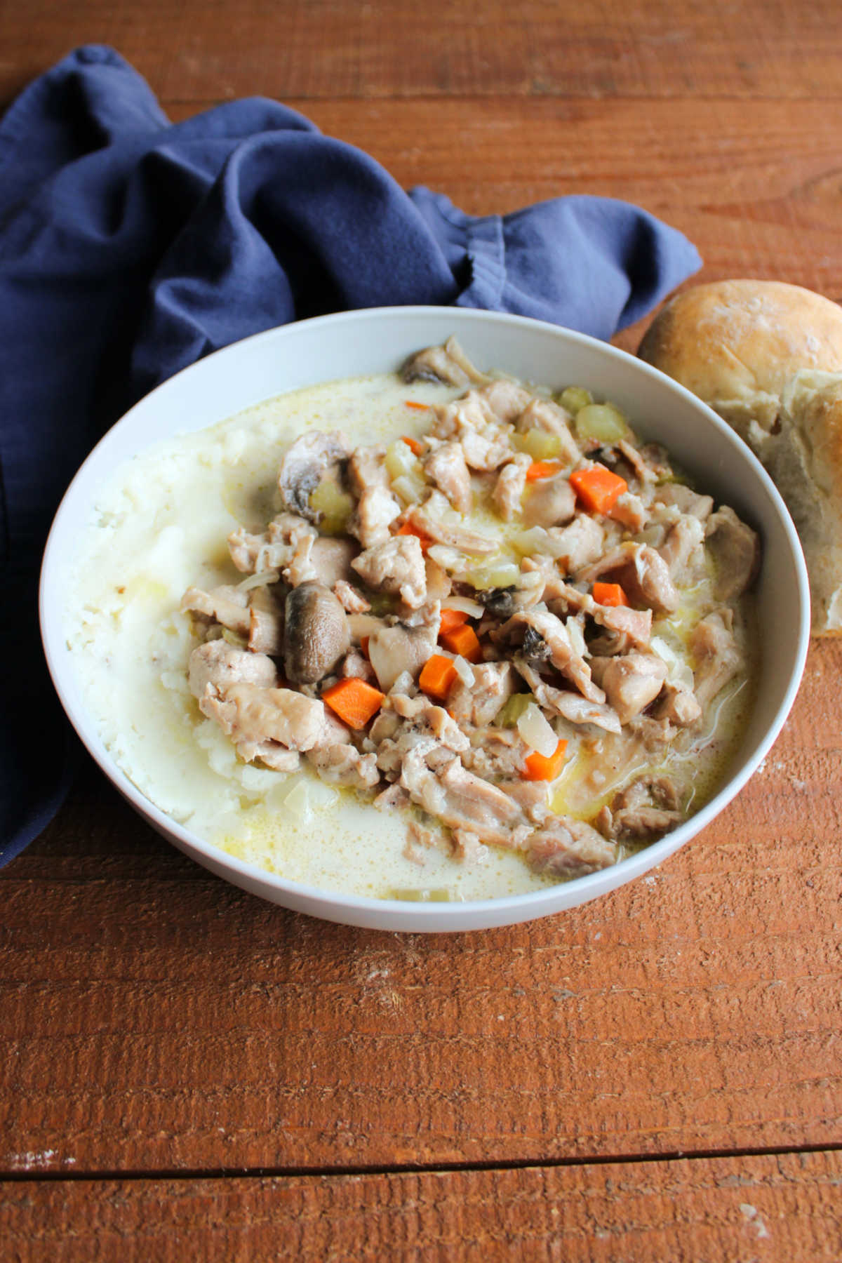 Bowl of creamy rabbit stew with chunks of rabbit, onion, carrot, and mushrooms served over mashed potatoes, ready to eat. 