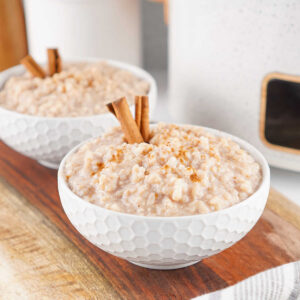 Two bowls of creamy rice pudding with cinnamon in front of the slow cooker they were cooked in.