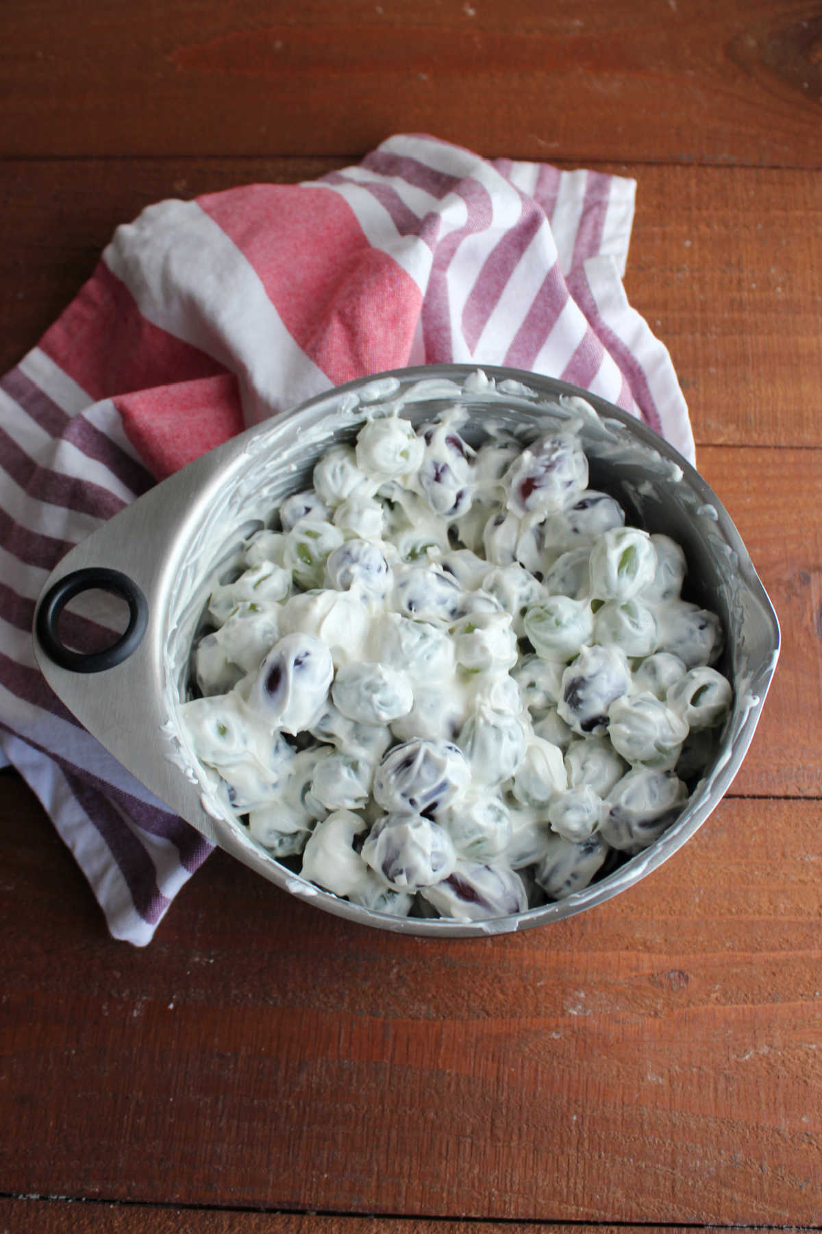 Mixing bowl filled with red and green grapes coated in creamy dressing, ready to be transferred to a serving dish and topped with brown sugar and pecan topping. 