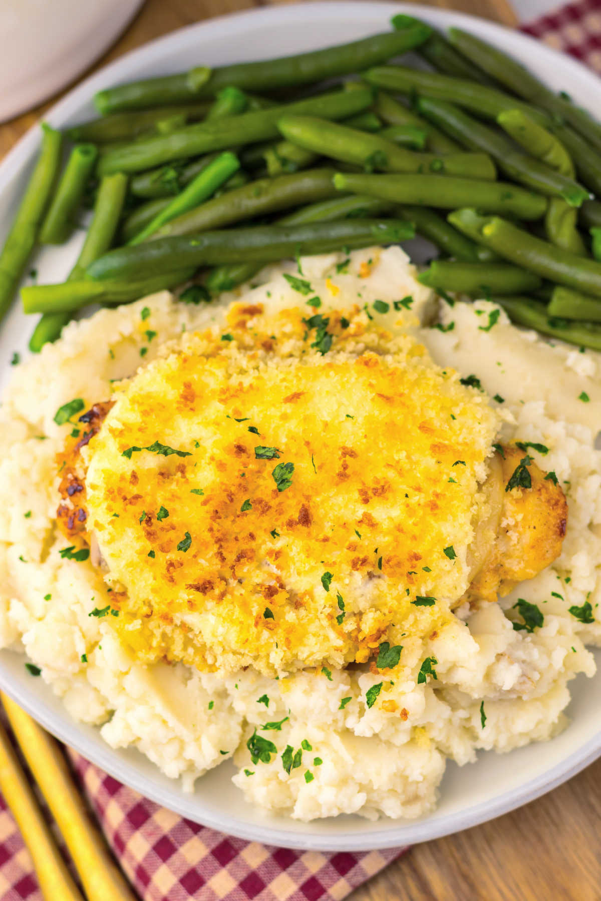 Close up of dinner plate filled with green beans and mashed potatoes topped with a parmesan crusted chicken breast. 