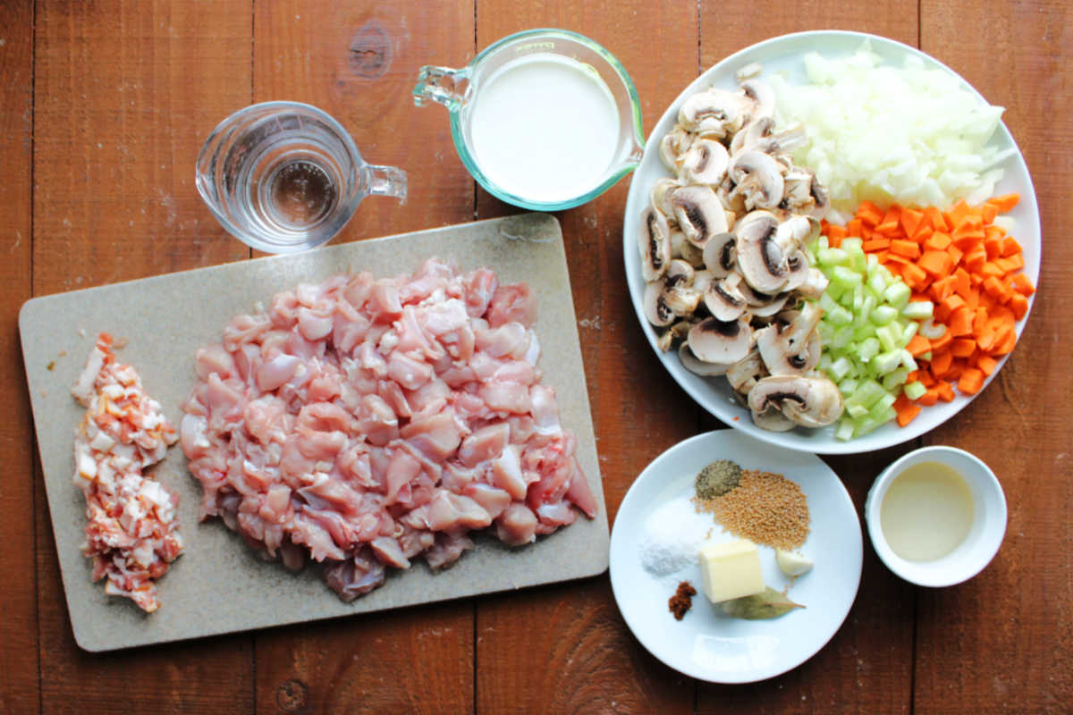 Ingredients including bacon, rabbit meat, water, cream, white wine vinegar, mushrooms, carrots, onions, and spices ready to be made into a creamy German style rabbit stew. 