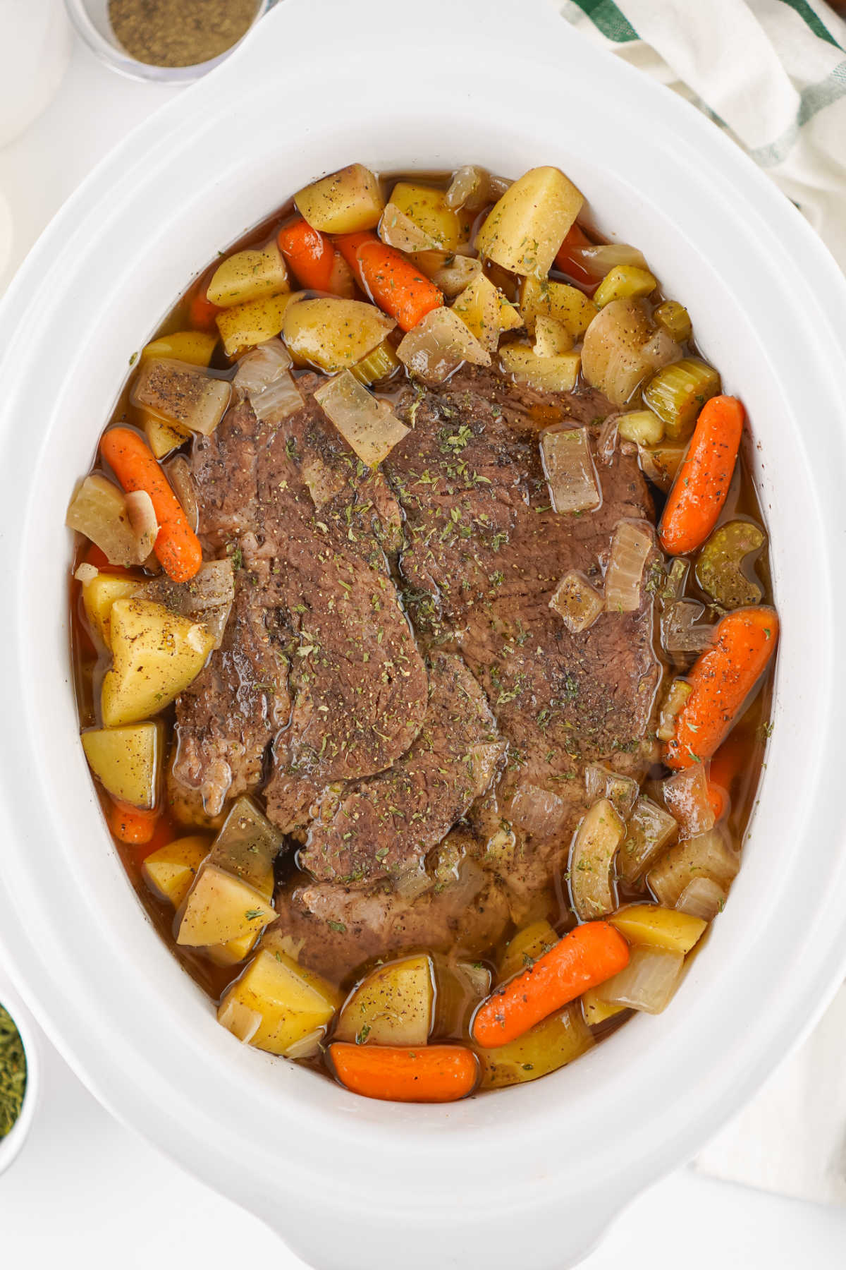 Crockpot filled with cooked pot roast with tender cooked chuck roast surrounded by cooked carrots, chunks of potato, celery, and onions in broth. 