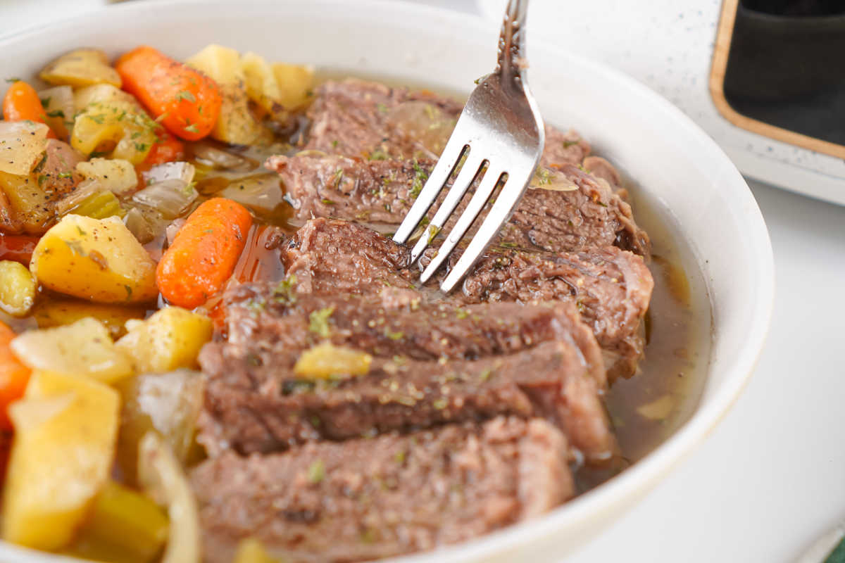 Fork getting a bite of tender roast beef from a bowl of slow cooker pot roast. 