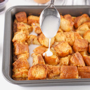 Donut Bread Pudding 14 Spoon drizzling powdered sugar glaze over pan of hot donut bread pudding.