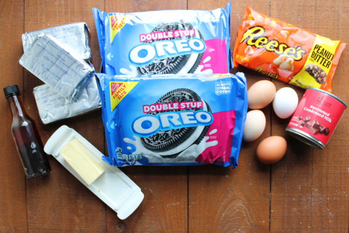 Ingredients including cream cheese, Oreos, peanut butter chips, sweetened condensed milk, eggs, butter and vanilla ready to be made into a peanut butter Oreo Cheesecake. 
