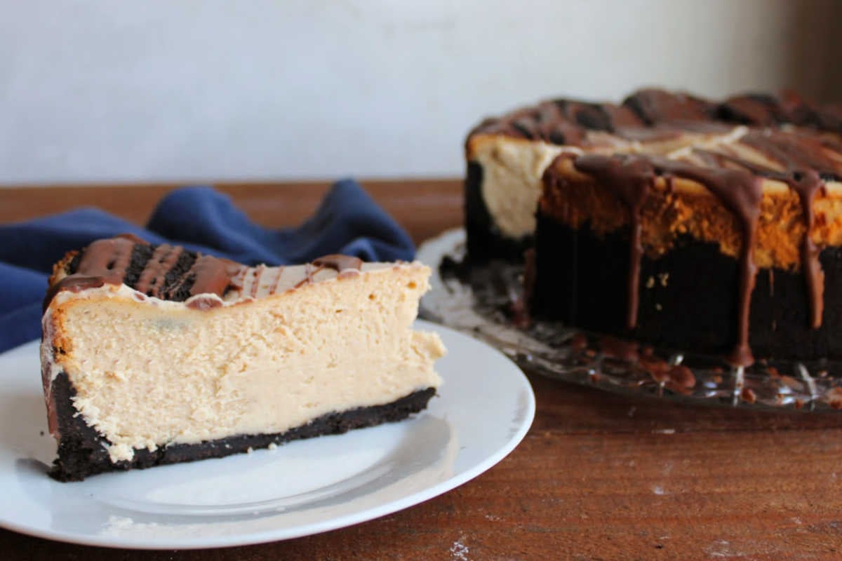 Slice pf peanut butter cheesecake with Oreo crust and Oreos on a dessert plate next to the remaining cheesecake. 