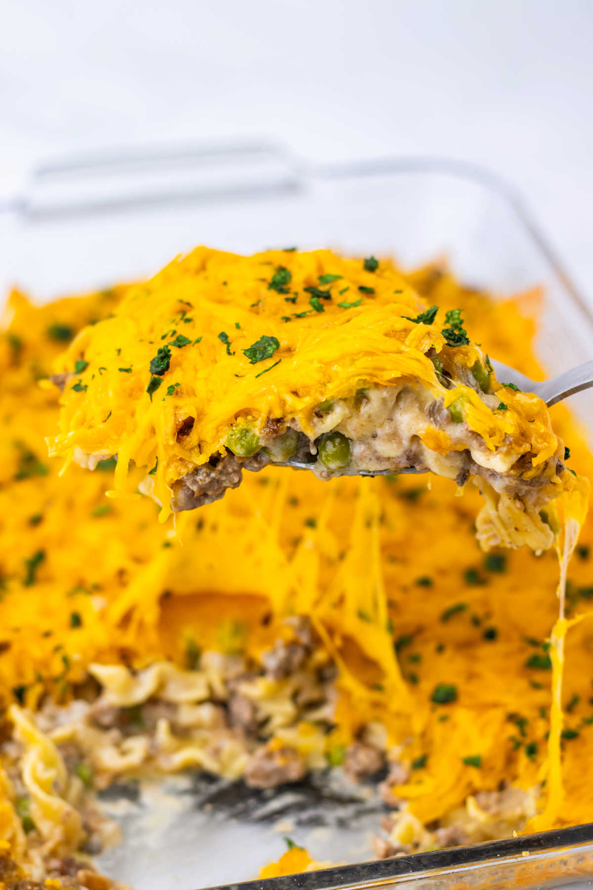 Amish Country Casserole 8 Serving spoon scooping a helping of amish country casserole with lots of melted cheese on top out of the casserole dish.