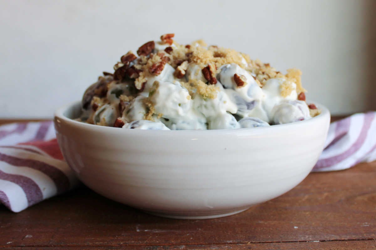 Serving bowl piled high with grape salad in thick creamy dressing topped with pecans and extra brown sugar, ready to be served. 
