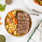 Plate with slices of roast beef served with cooked carrots, potatoes, celery, and onions in gravy.