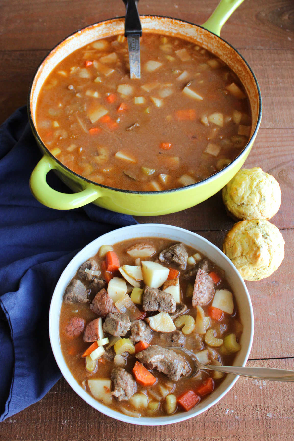 Pot of homemade venison stew next to a bowl of stew with savory muffins, ready to eat. 