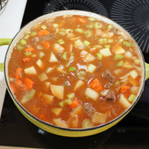 Pot full of venison stew mixture after the broth, water, and tomato juice have been added, ready to simmer and thicken.