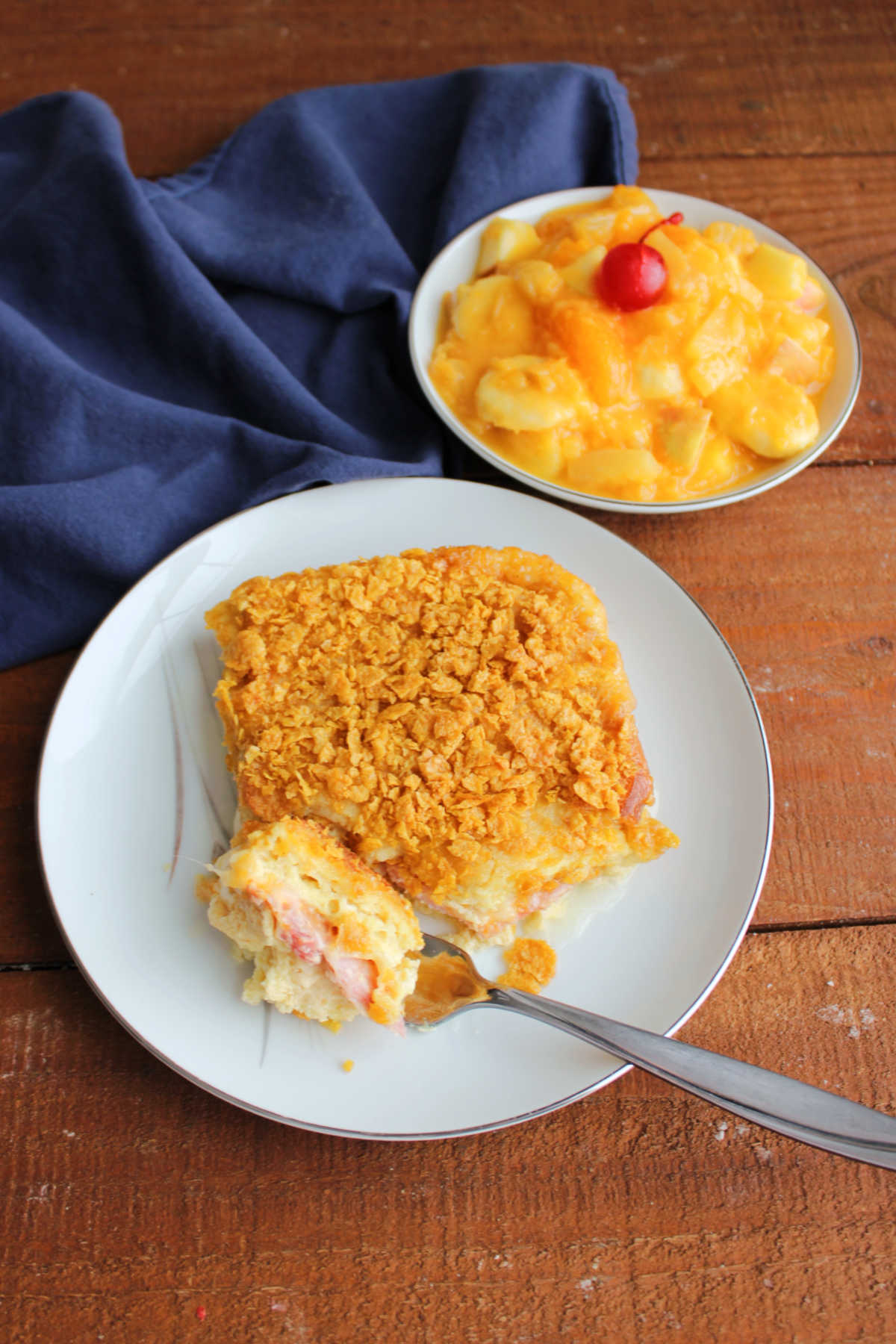 Hot Ham Sandwich Breakfast Bake 8 Bite of ham sandwich breakfast casserole on fork showing ham and melty cheese between pieces of egg soaked bread served with a bowl of Tang fruit salad.