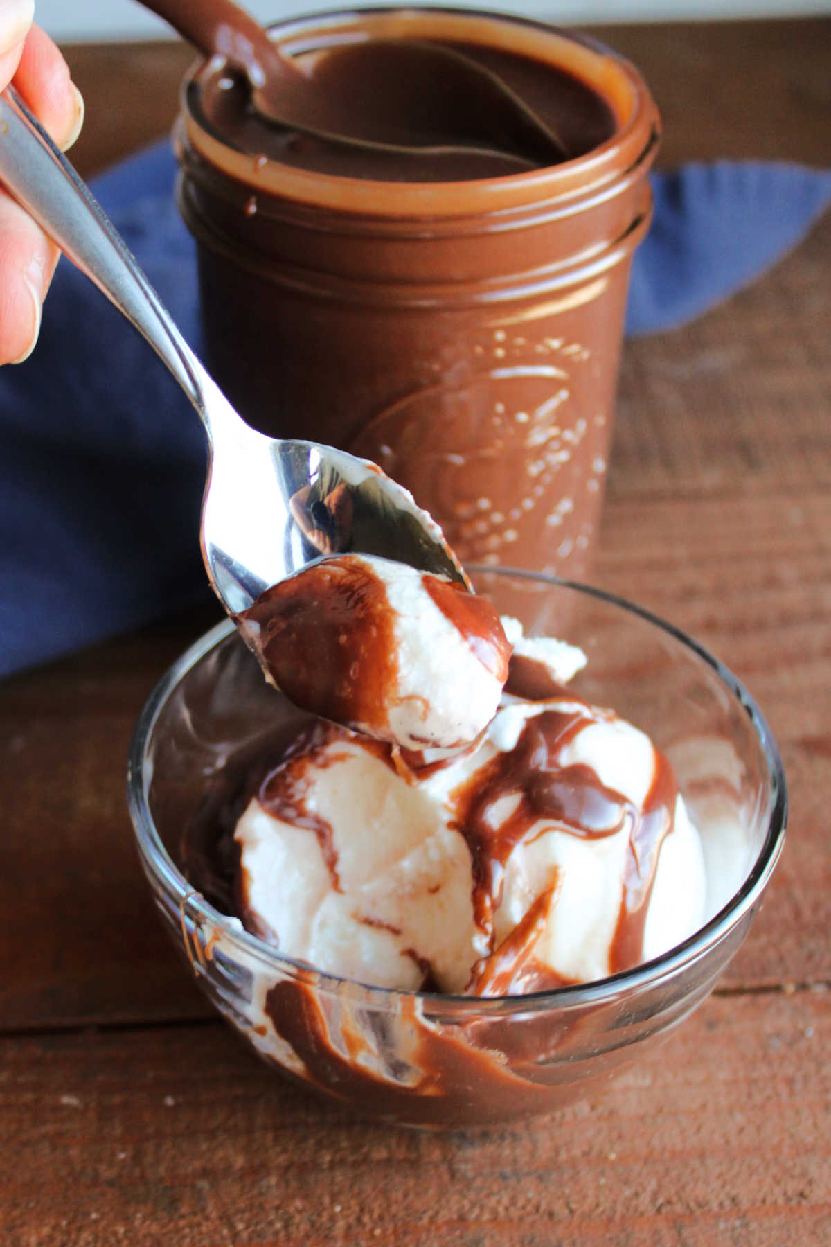 Bite of vanilla ice cream with hot fudge sauce on it on a spoon, ready to eat. 