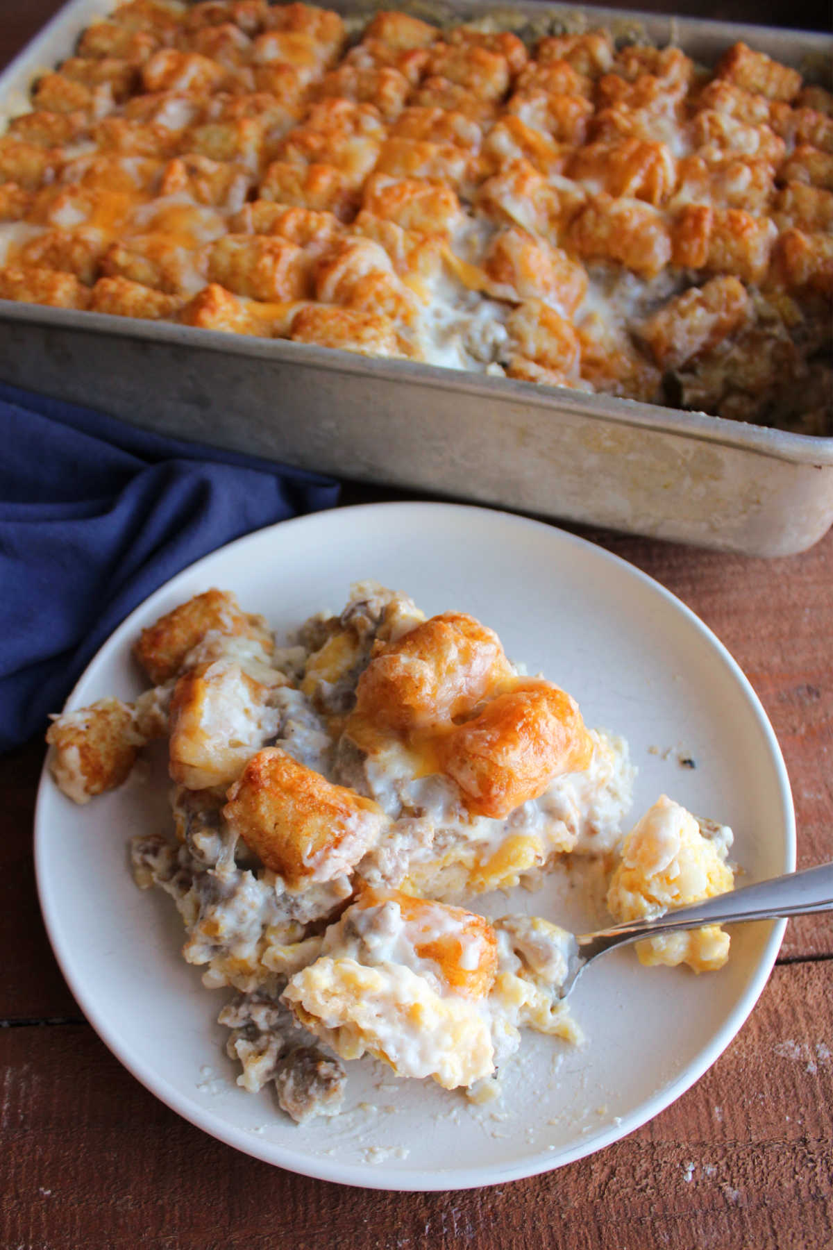 Biscuits and Gravy Tater Tot Casserole 7 Bite of breakfast casserole on fork showing the layers of biscuit on the bottom topped with eggs, sausage gravy, golden brown tater tots and melted cheese.