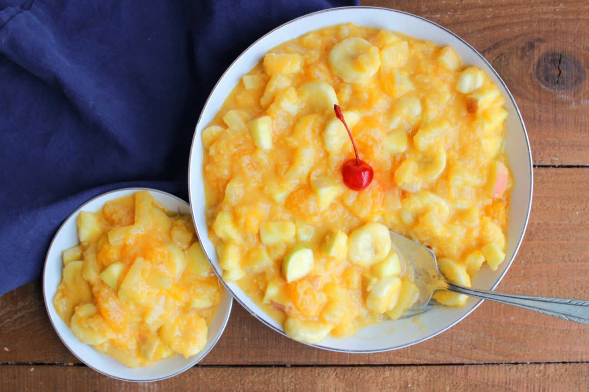 Tang Fruit Salad 5 Large serving bowl of Tang fruit salad topped with a maraschino cherry next to a smaller bowl with a serving of fruit salad in creamy orange dressing, ready to eat.
