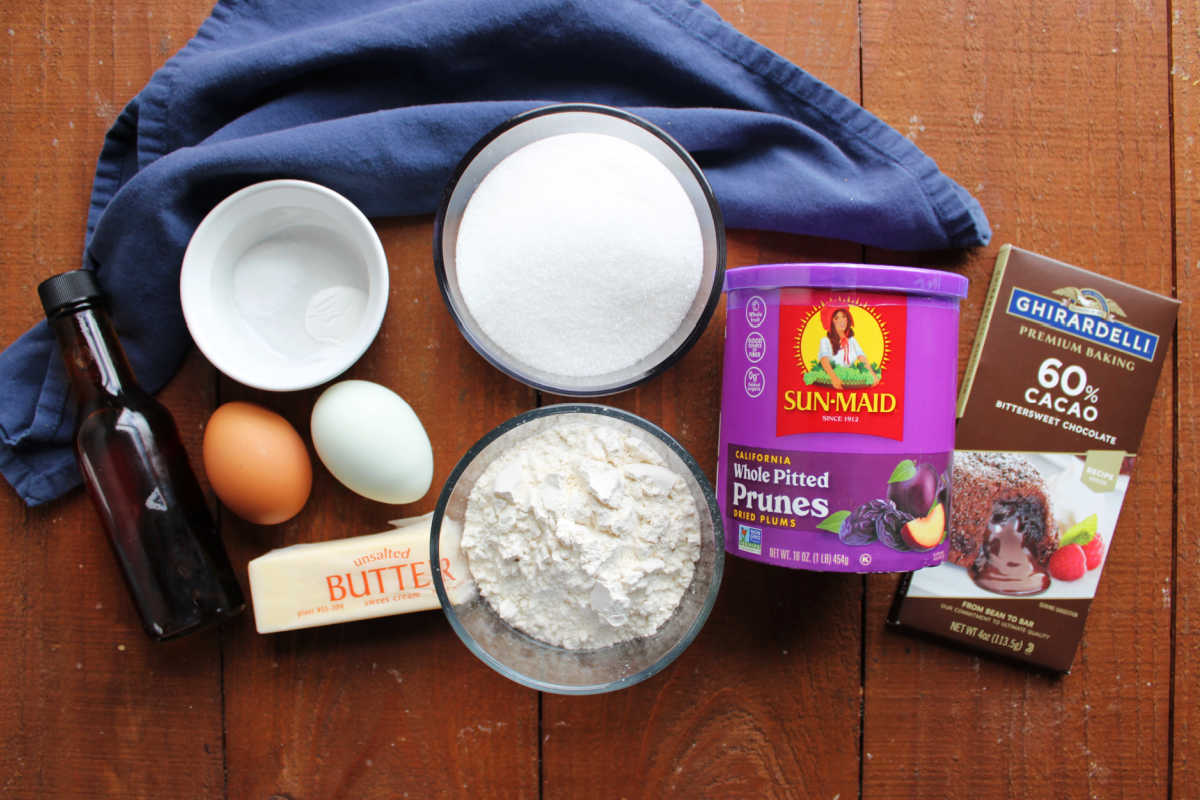 Ingredients including vanilla, eggs, butter, salt, baking powder, flour, sugar, prunes, and bittersweet chocolate ready to be made into prune brownies. 