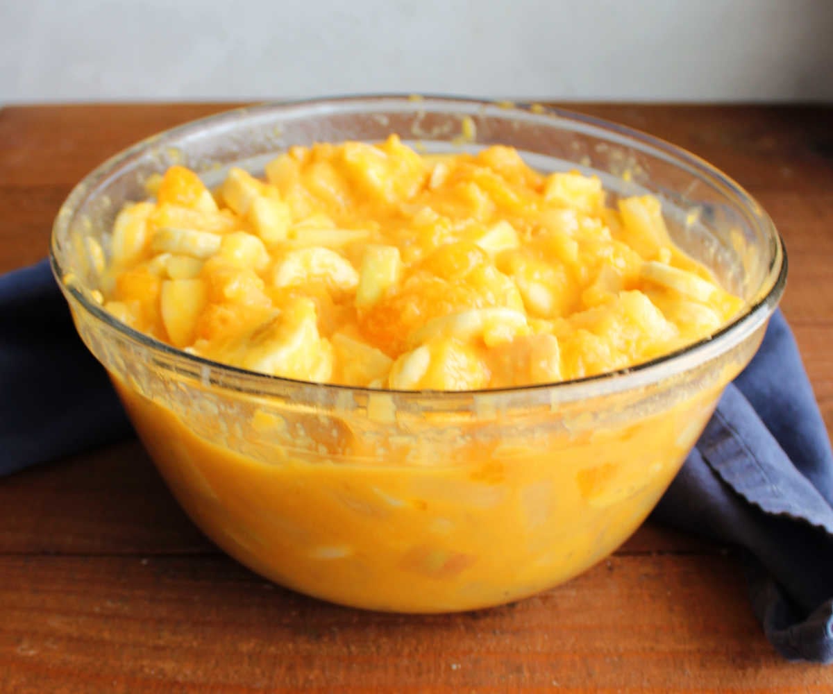 Tang Fruit Salad 7 Mixing bowl filled with fruit coated in creamy orange Tang dressing, ready to be chilled.