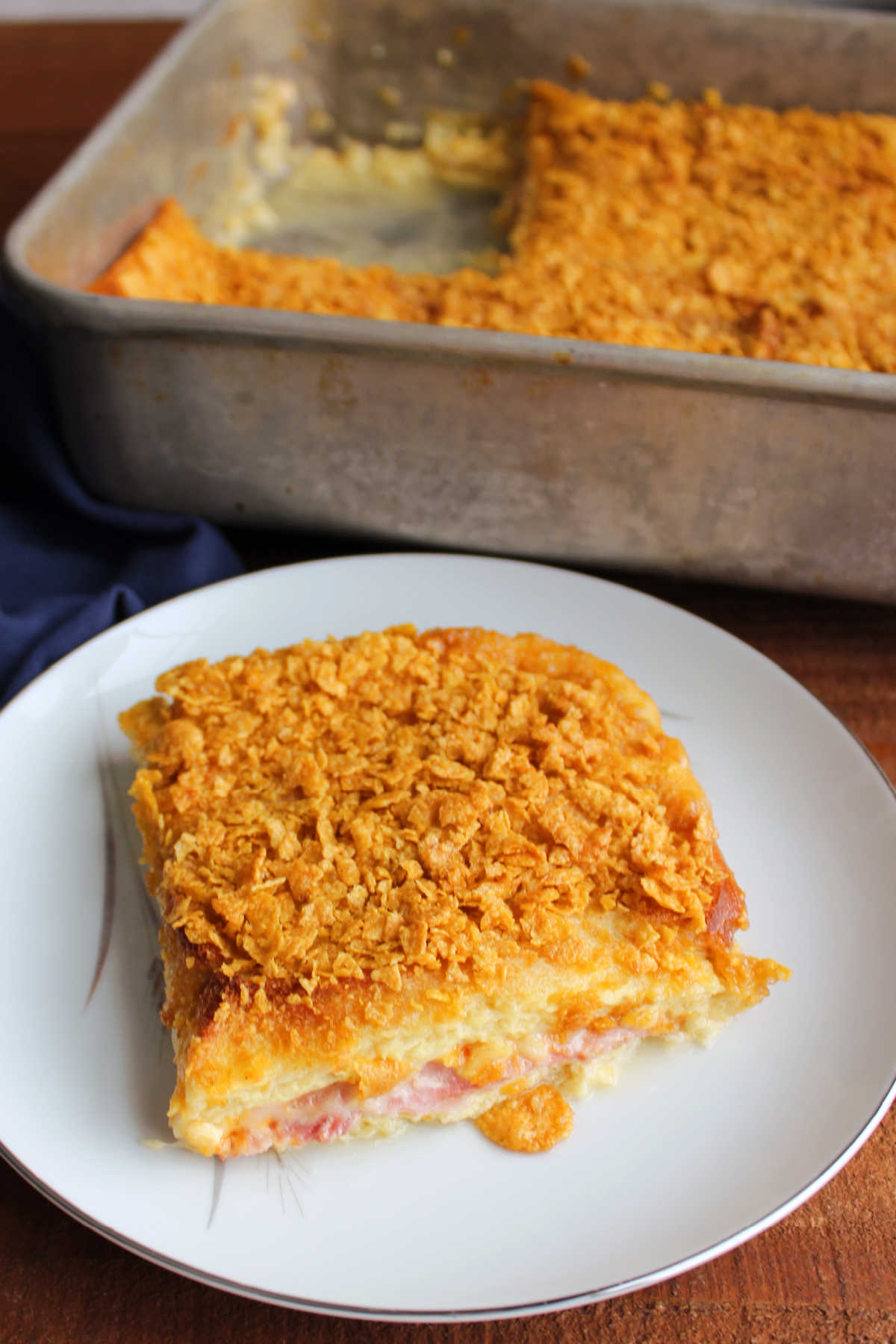 Hot Ham Sandwich Breakfast Bake 7 Hot ham sandwich baked in egg mixture and topped with golden cornflake crumbs on plate with remaining casserole in the background.